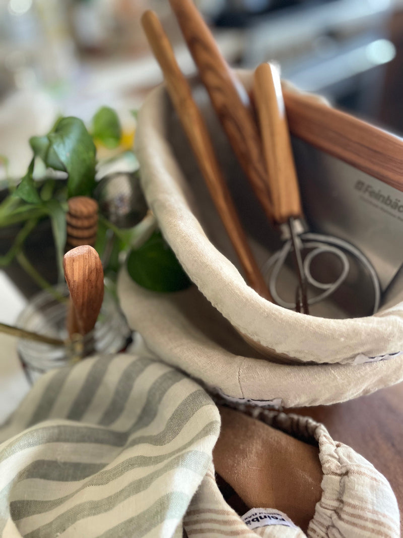 Shown are the essential Sourdough tools. Presented are 2 bannetons, a bench scraper, a danish dough whisk, an olive wood spurtle, linen bowl covers to cover dough. Also shown in picture is an olive wood butter knife and olive wood handled lame 