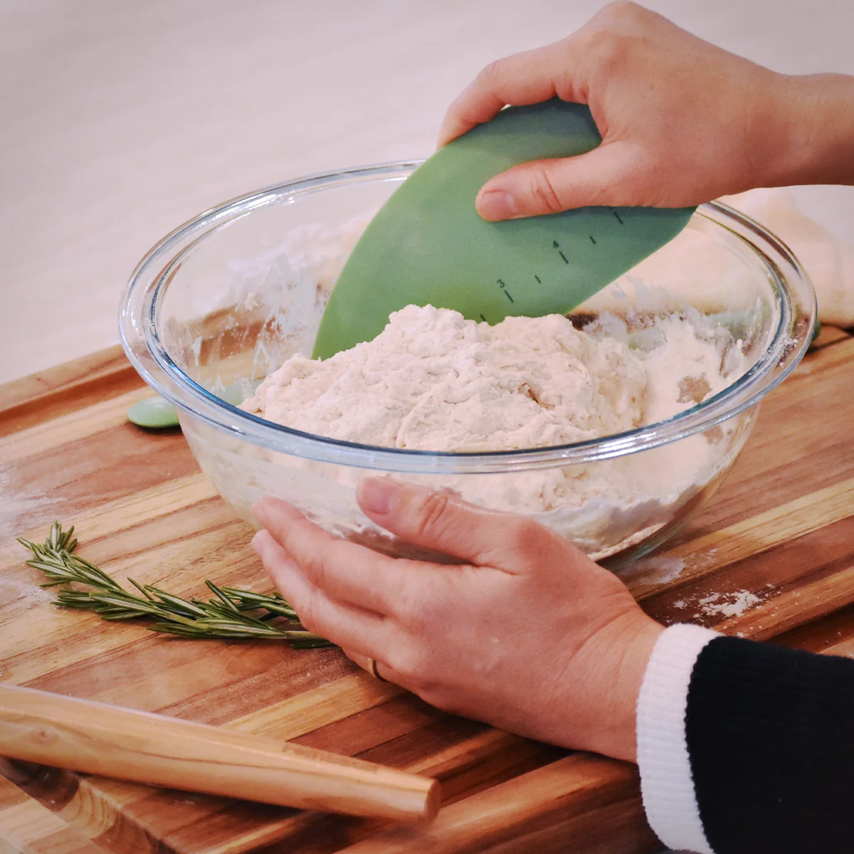 Hands using a green Feinbäck silicone bowl scraper to work sourdough in a glass bowl